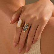 Close-up of a hand wearing two gold rings with gemstones on a neutral background