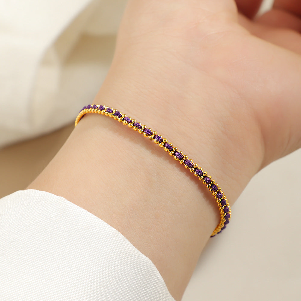 Gold and purple cord bracelet worn on the wrist