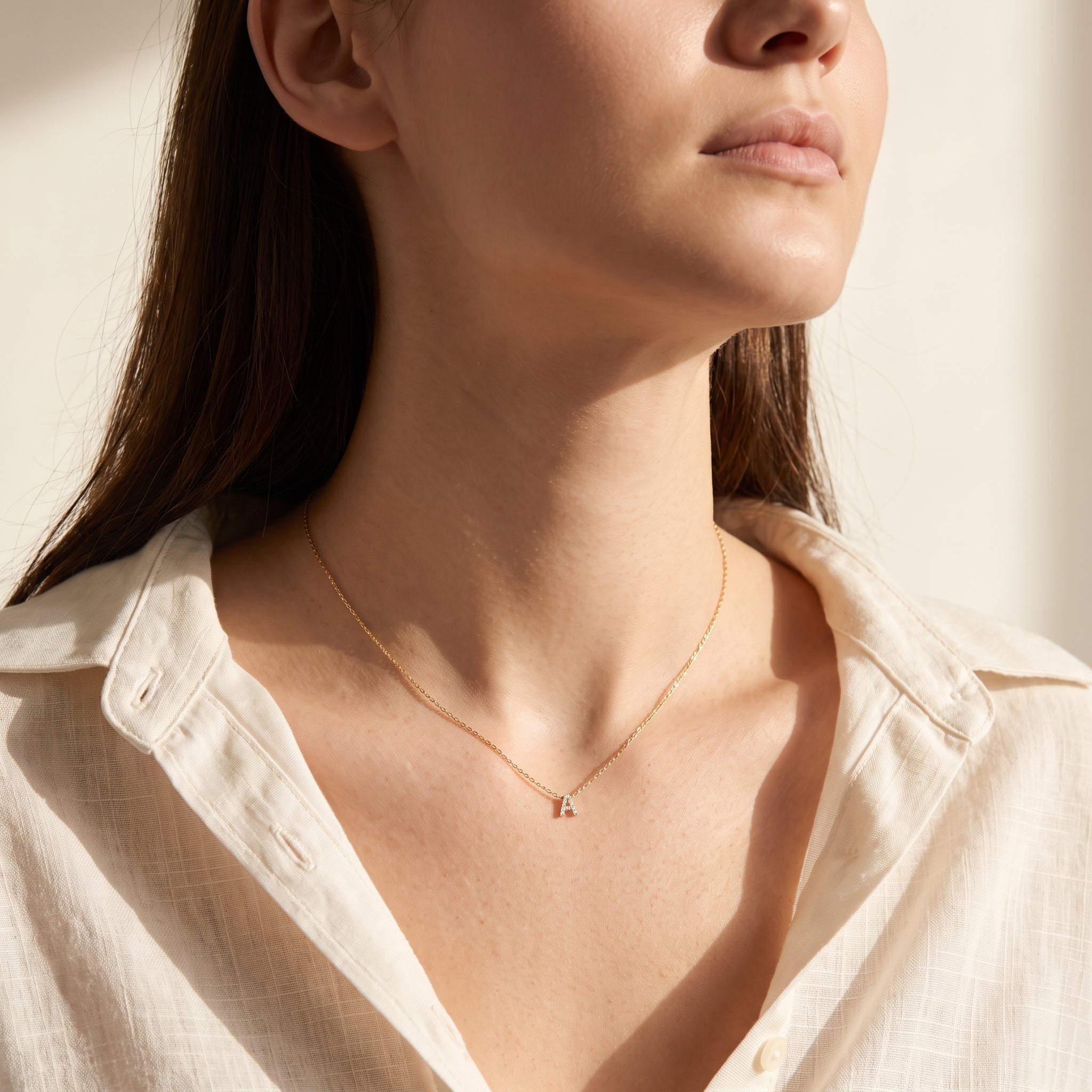 Woman in an ivory linen shirt wearing a dainty gold letter A necklace
