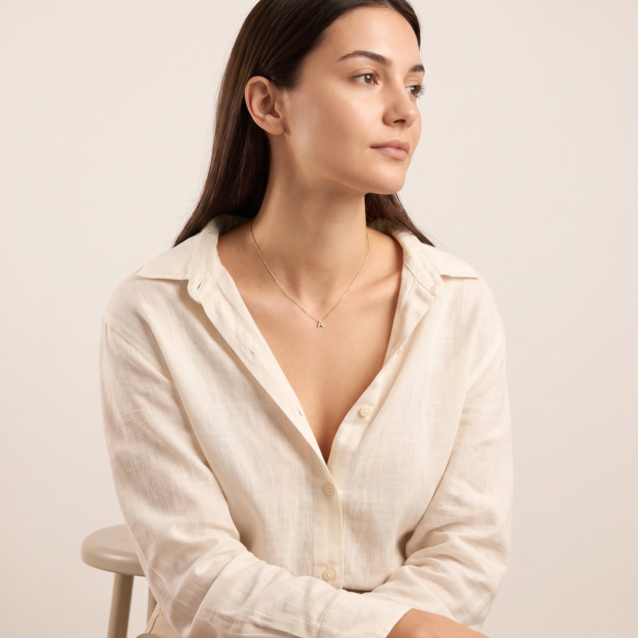 Seated woman in an ivory shirt wearing a small gold initial necklace