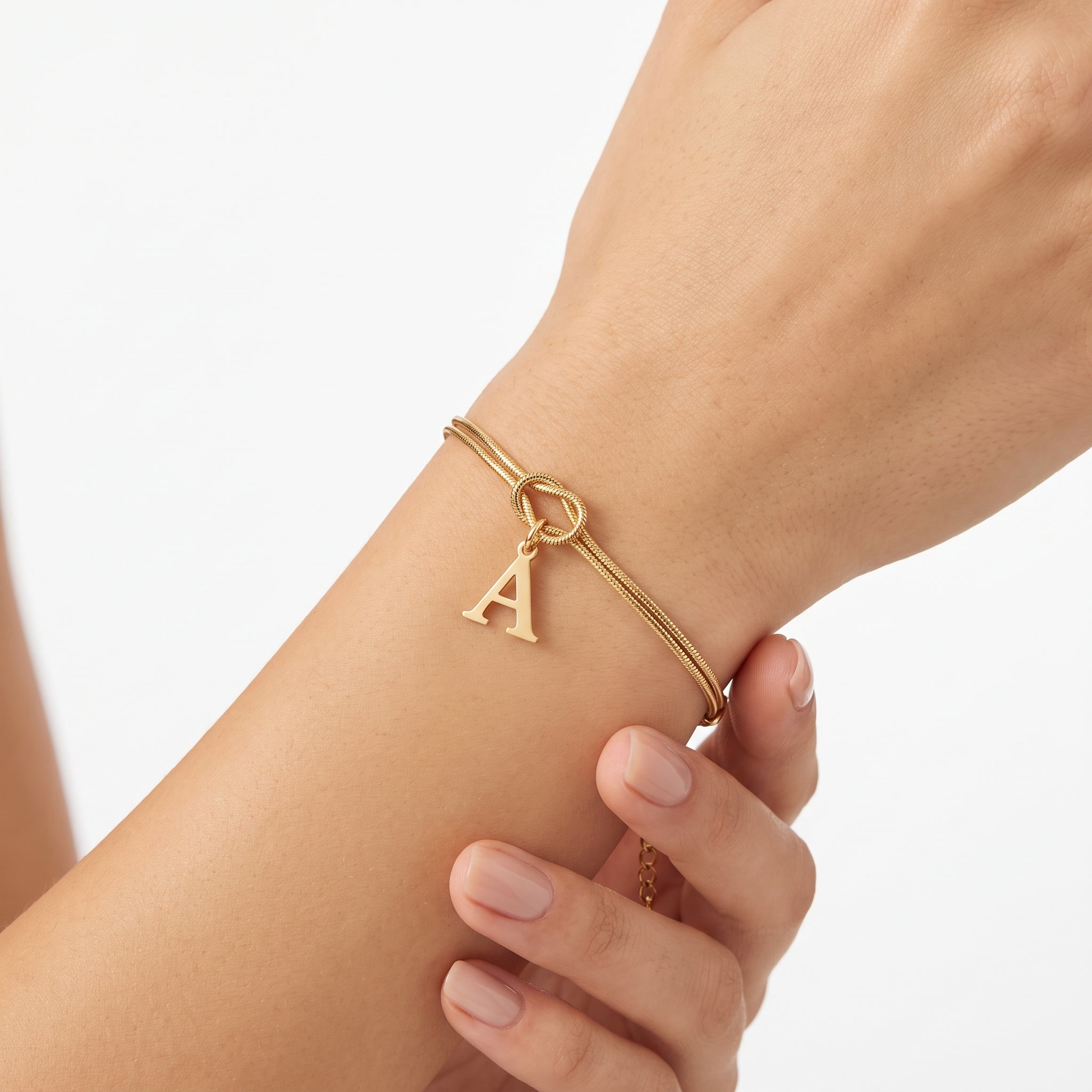 Gold letter initial bracelet with a knot charm worn on the wrist