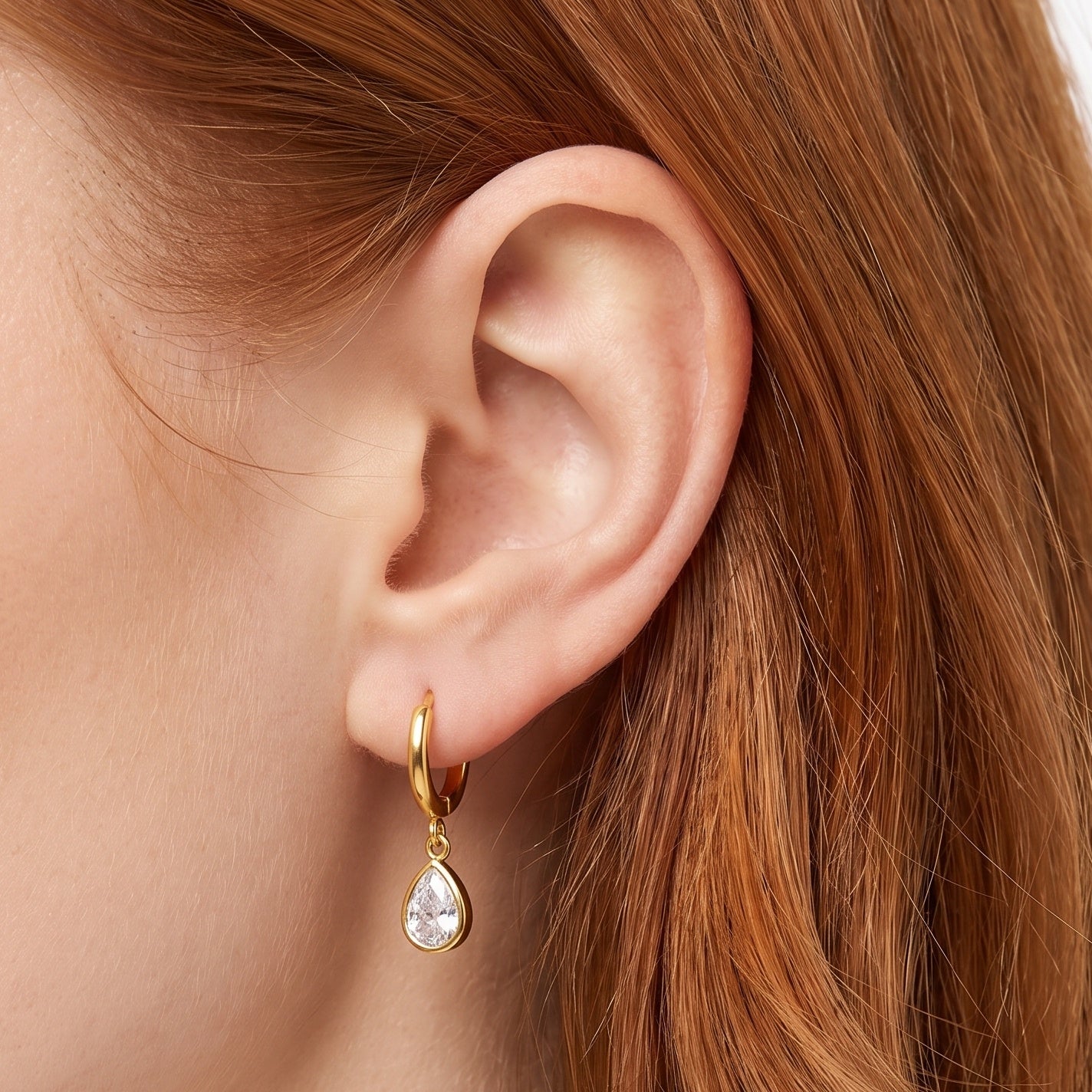 Gold huggie drop earrings with teardrop crystals worn on the ear