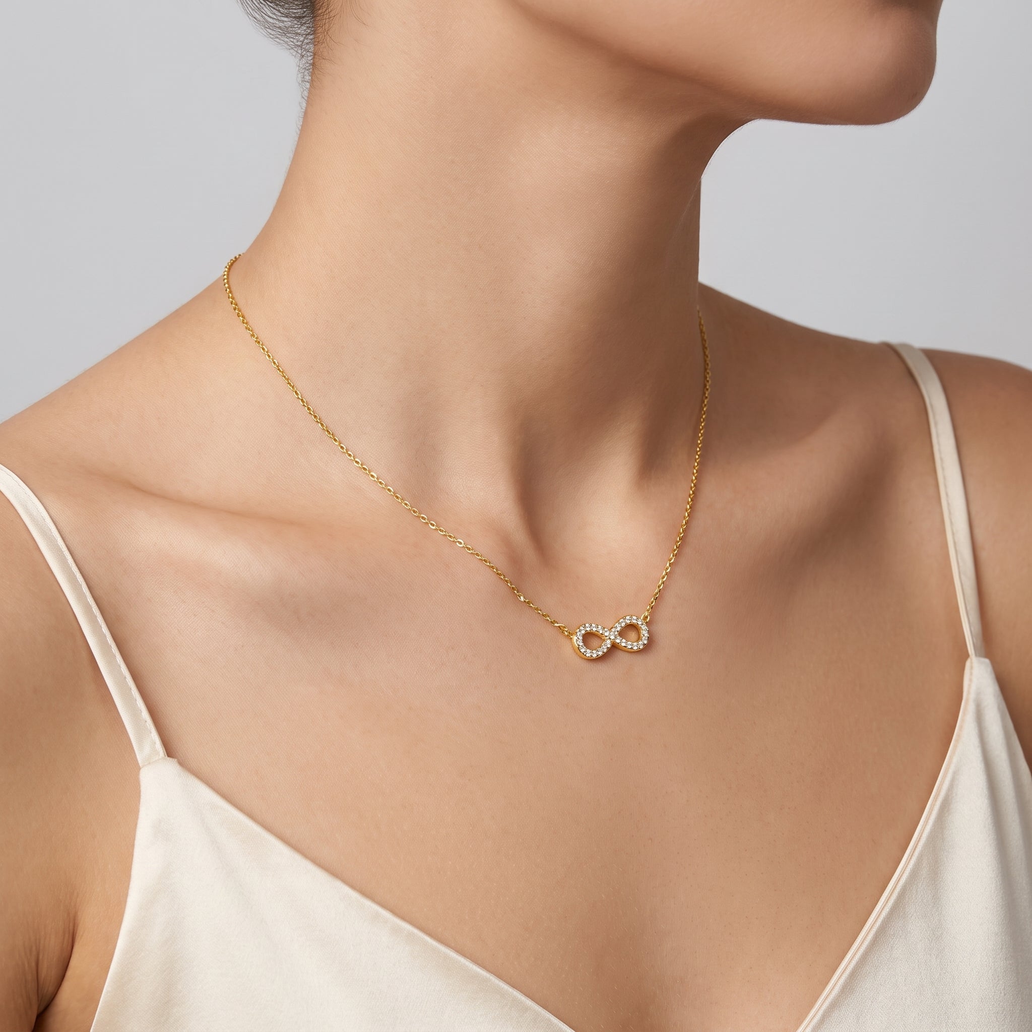 Gold pavé infinity necklace at the collarbone, a cream slip dress