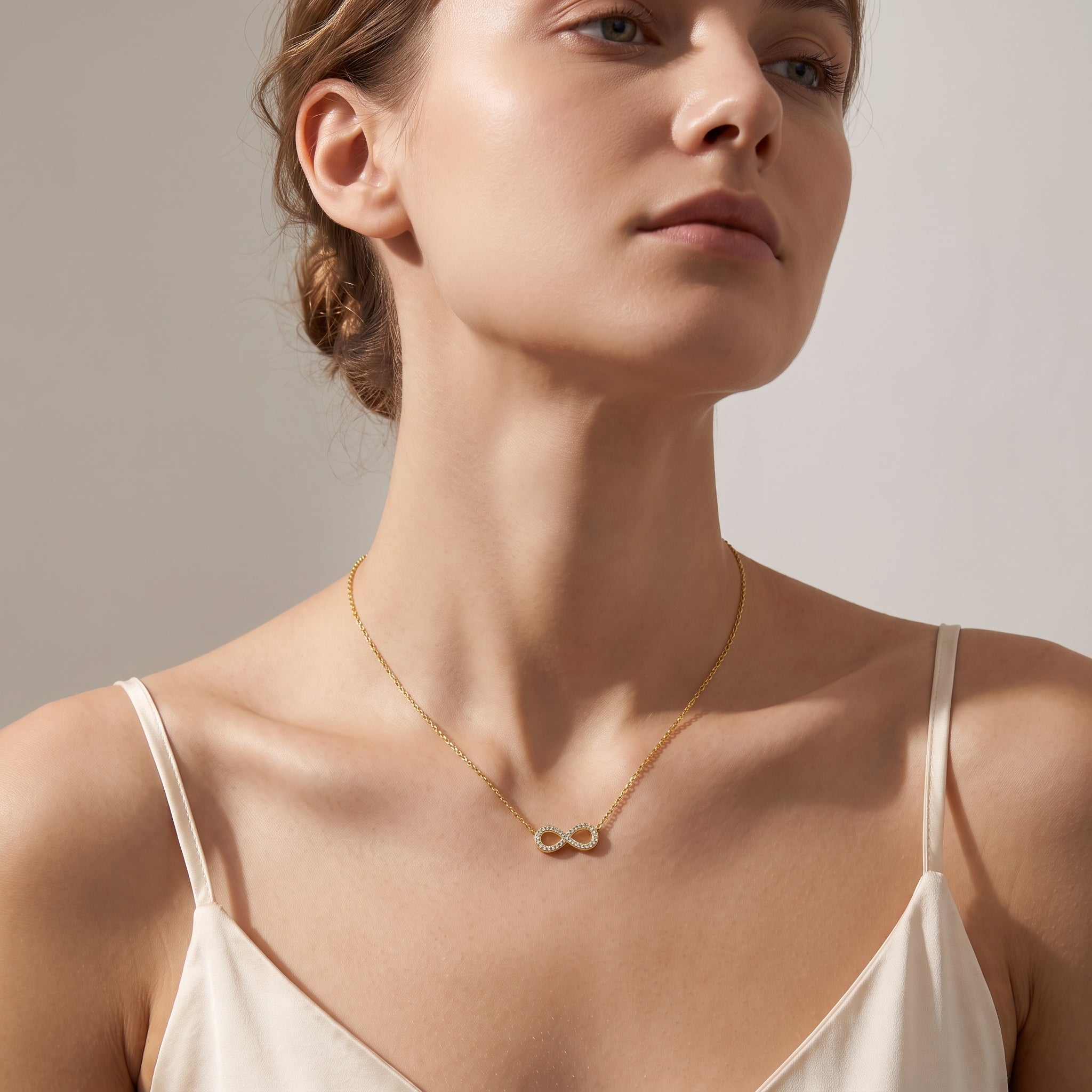 Gold pavé infinity necklace worn, seen from a low angle