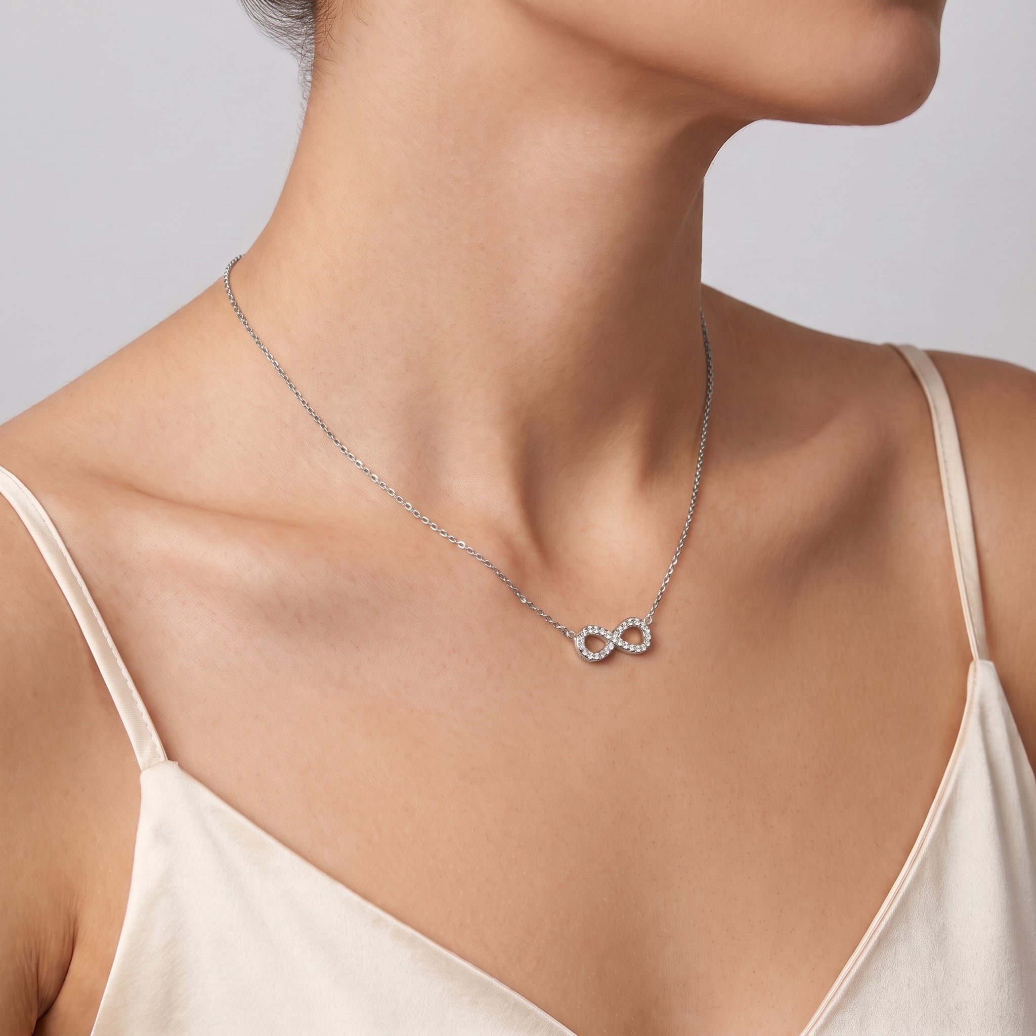 Silver pavé infinity necklace at the collarbone, a cream slip dress