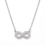 Silver pavé infinity necklace laid out on a white background