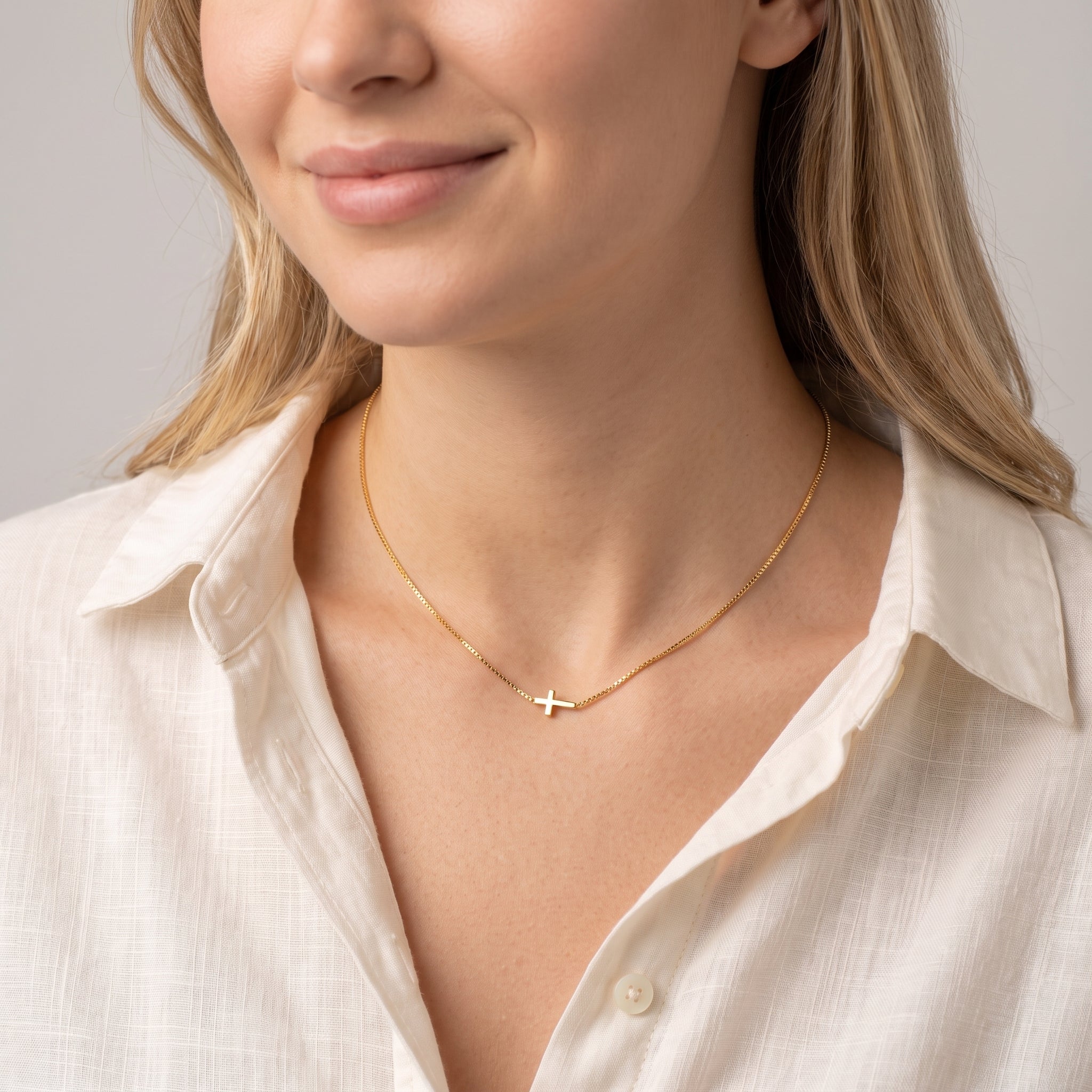 Gold sideways cross necklace worn with the head tilted down