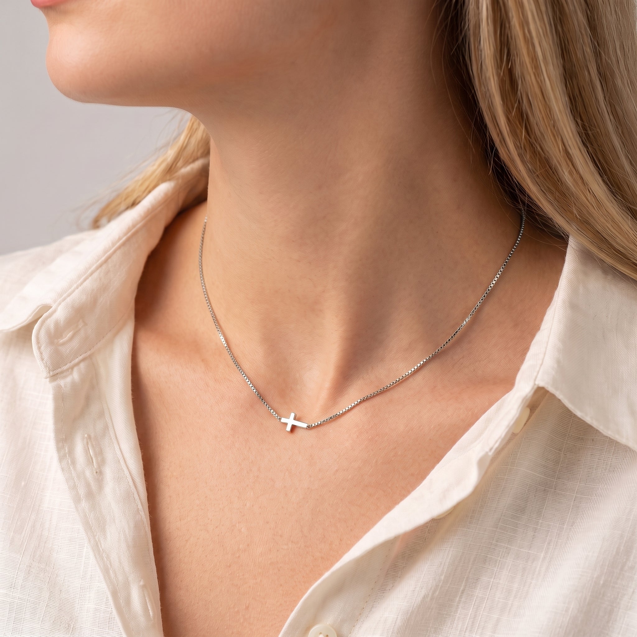 Silver sideways cross necklace at the collarbone, an ivory linen shirt