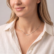 Silver sideways cross necklace worn with the head tilted down