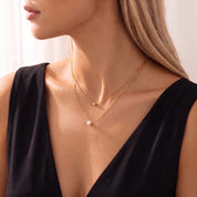 Three-quarter profile of a gold double chain necklace with a single pearl