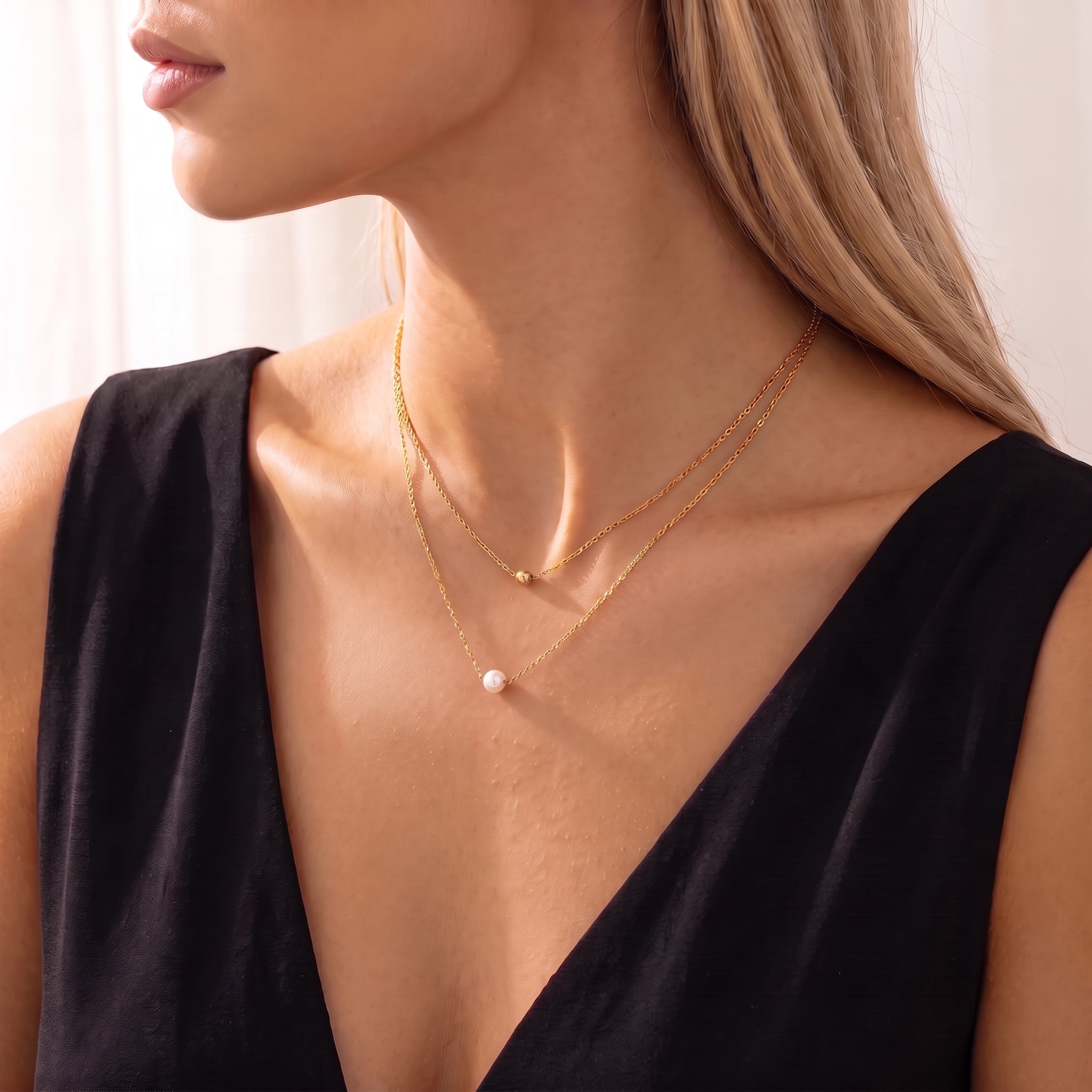 Three-quarter profile of a gold double chain necklace with a single pearl