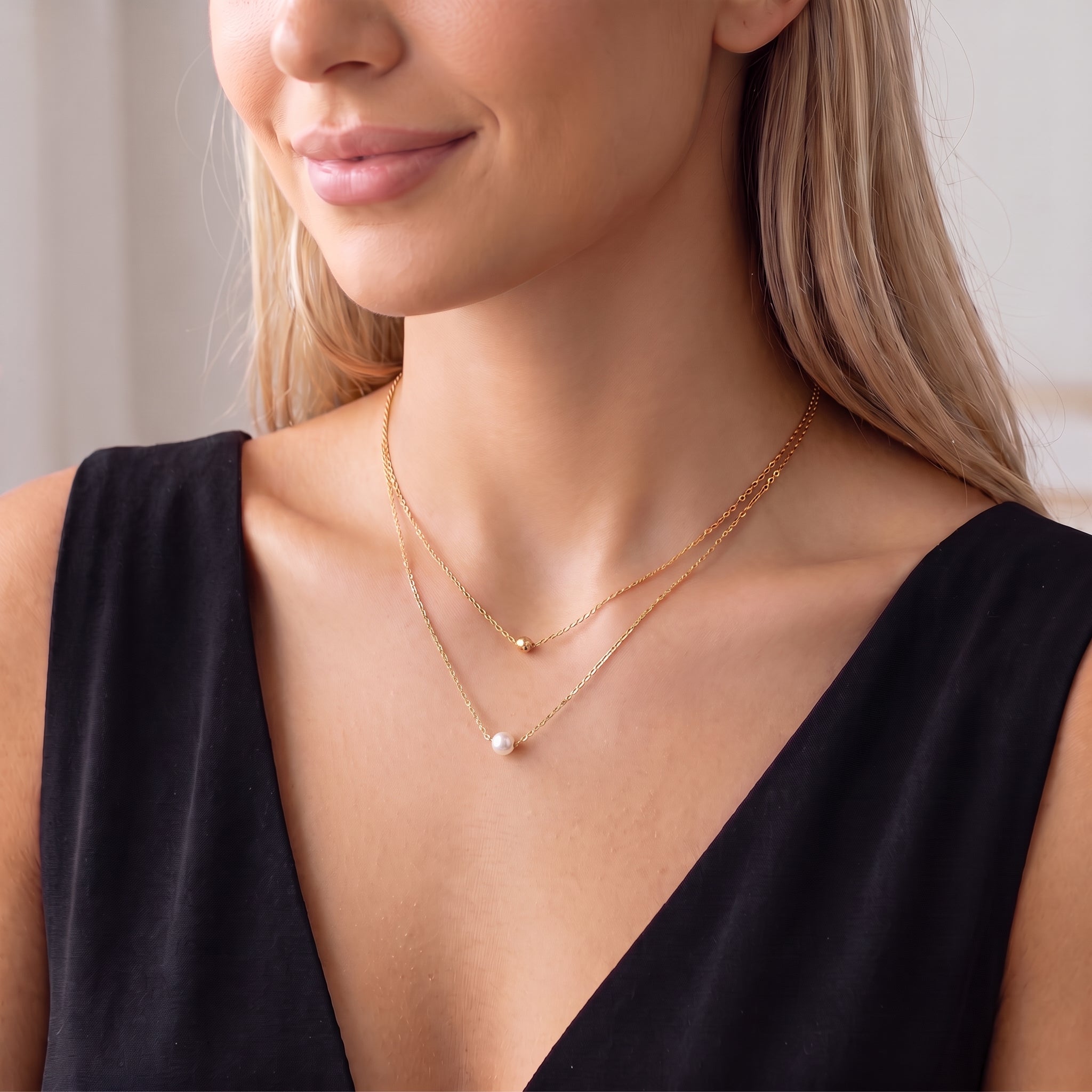 Smiling woman in a black dress wearing a dainty gold bead and pearl necklace