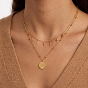 Woman wearing Celestine gold layered cross necklace with a north star coin pendant