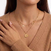 Hand at shoulder beside Celestine gold cross charm necklace and beaded chain