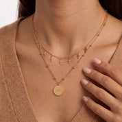 Fingers near the collarbone framing tiny gold cross charms and a star medallion