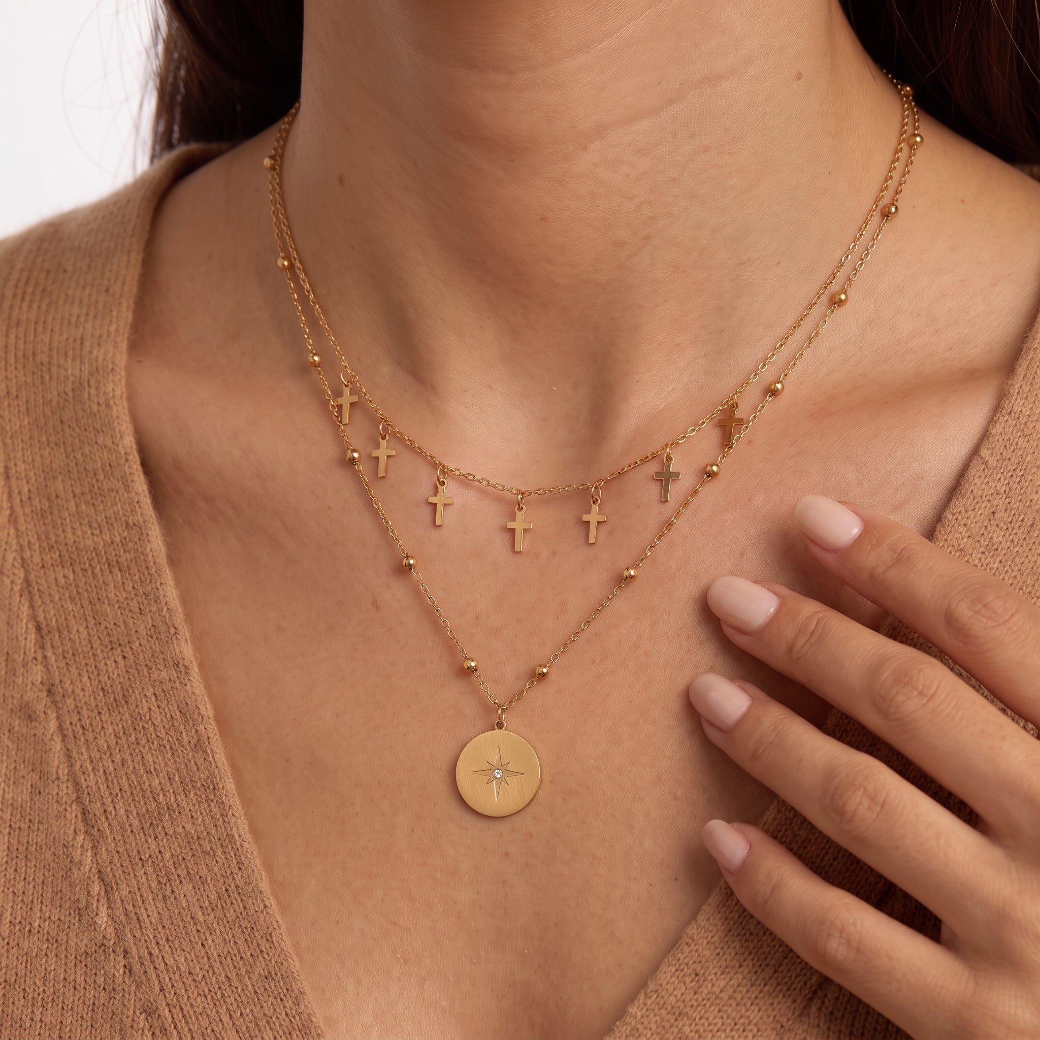 Fingers near the collarbone framing tiny gold cross charms and a star medallion