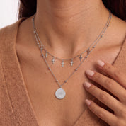 Fingers near the collarbone framing tiny silver cross charms and a star medallion