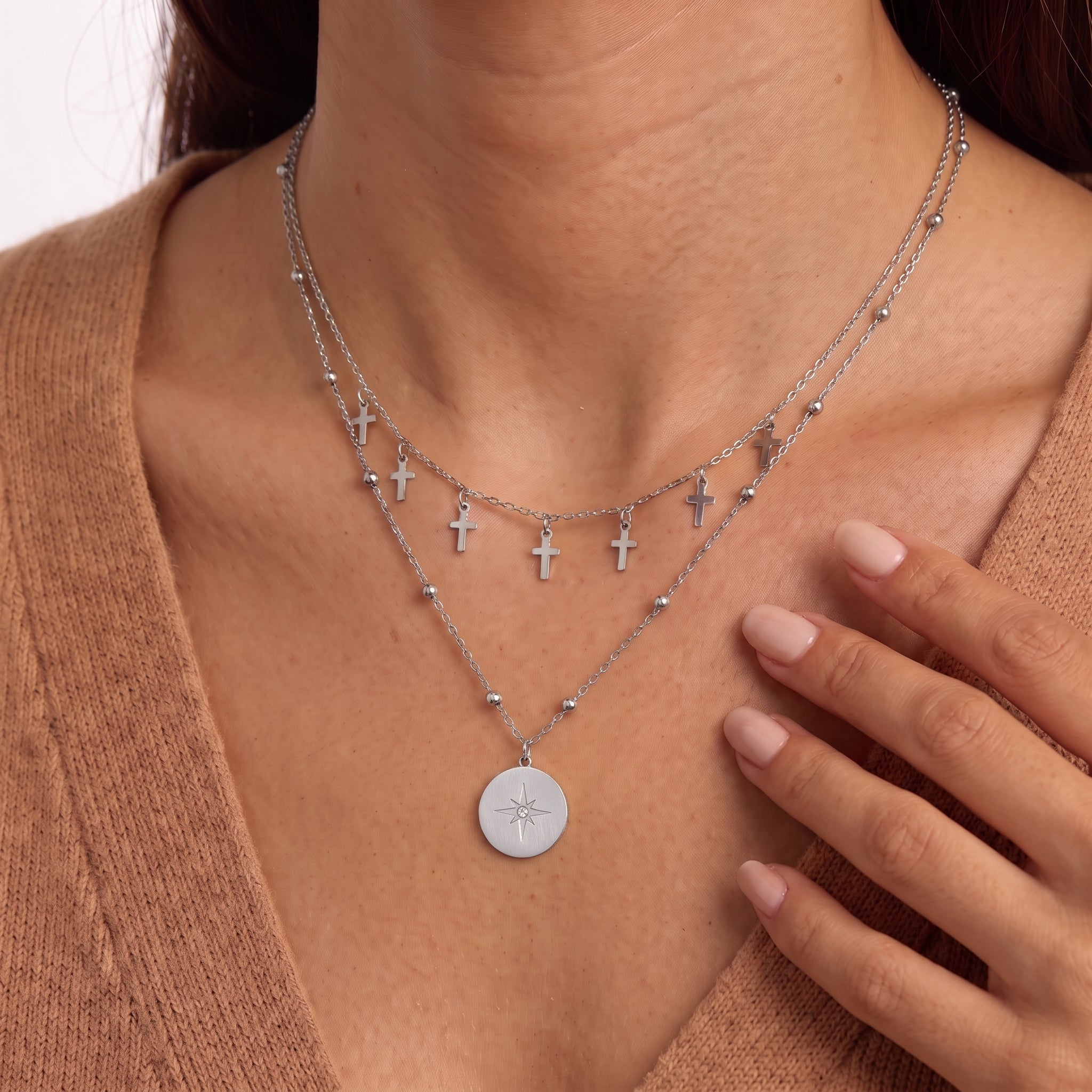 Fingers near the collarbone framing tiny silver cross charms and a star medallion