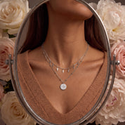 Celestine silver necklace reflected in an oval mirror, worn with a camel V-neck sweater