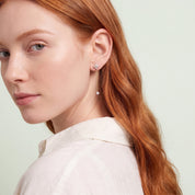 Red-haired woman glancing over her shoulder wearing Clarisse clover drop earring and ivory shirt