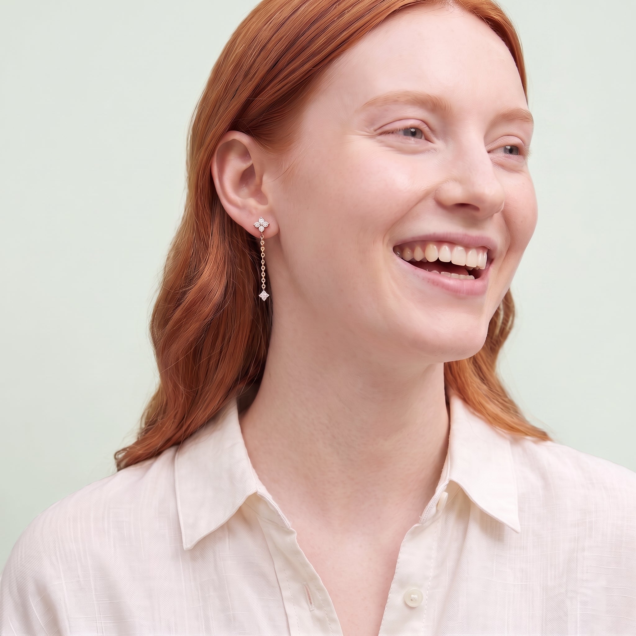 Laughing woman wearing gold Clarisse chain drop earring against a pale sage background