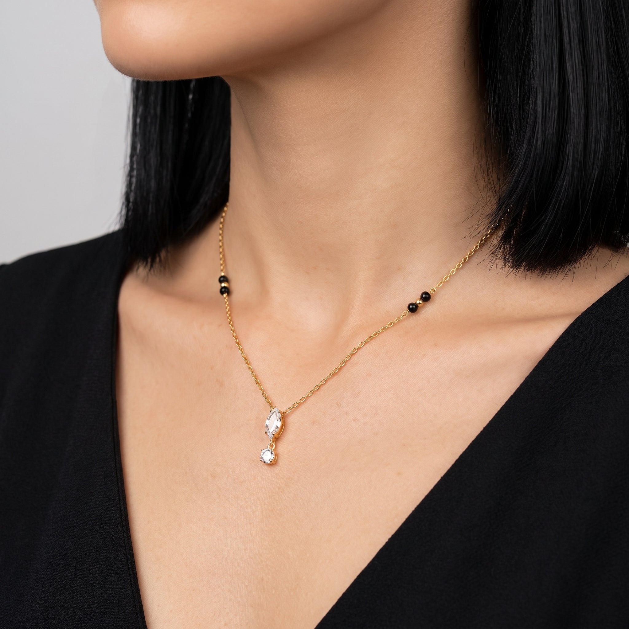 Gold crystal drop necklace at the collarbone, a black V-neck dress