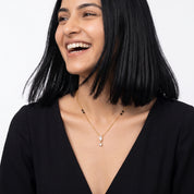 Gold crystal drop necklace worn while laughing, a black V-neck dress