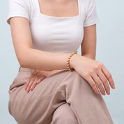 Seated woman in white square-neck top wearing Coralie gold heart bracelet
