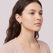 Gold square huggie earring worn with a blush cardigan
