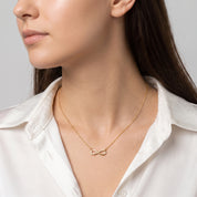 Gold infinity necklace at the collarbone, a white silk shirt