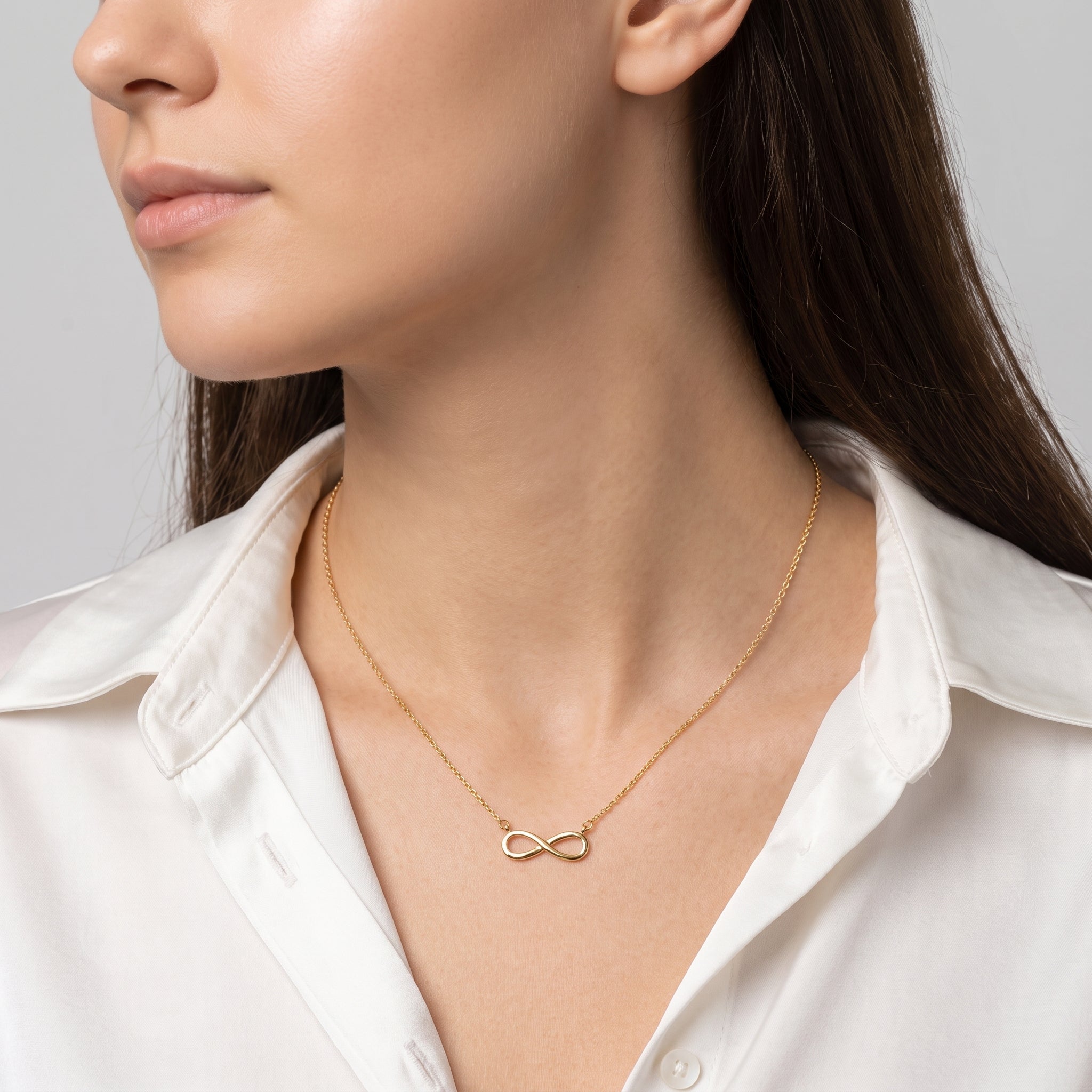 Gold infinity necklace at the collarbone, a white silk shirt