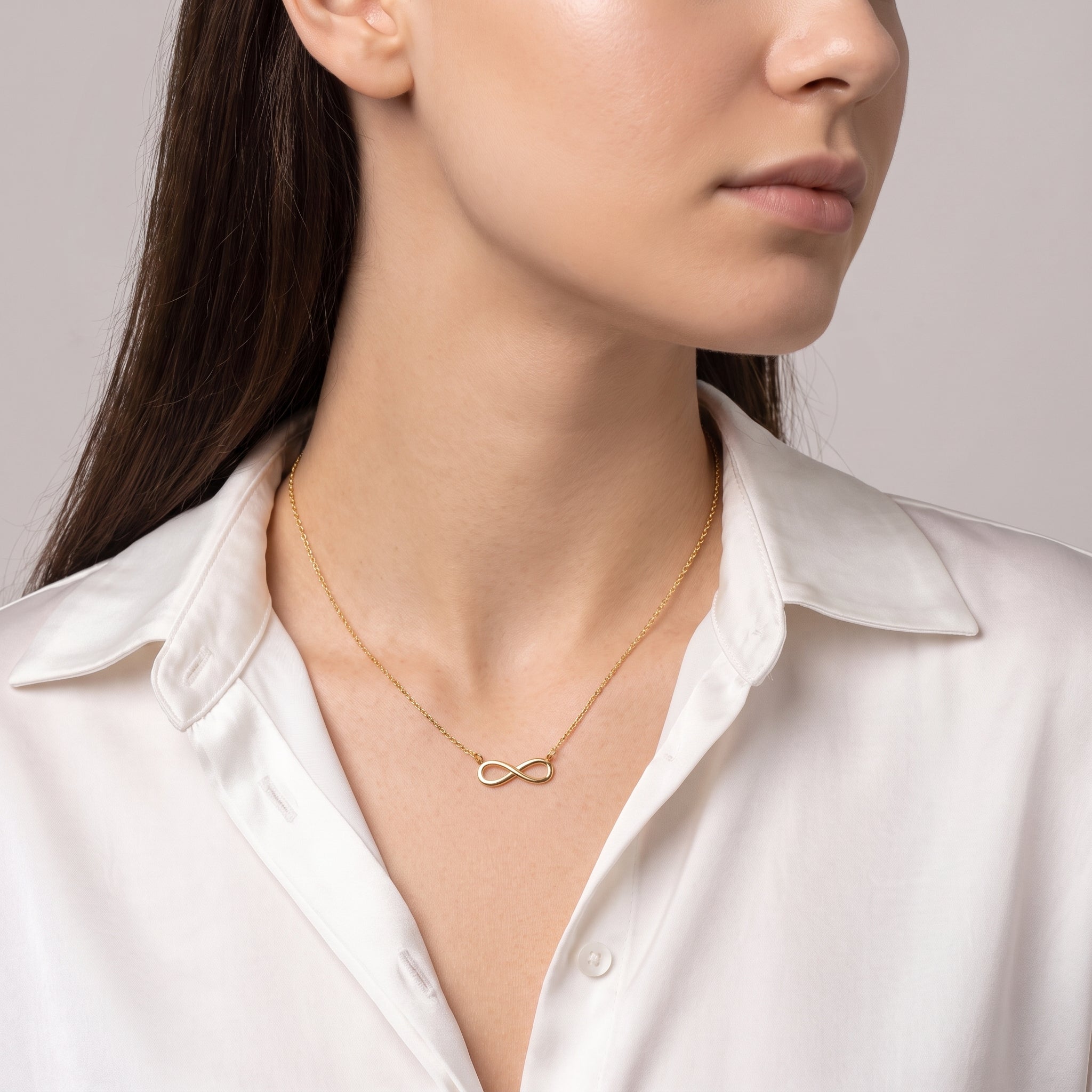 Gold infinity necklace worn with a glance over the shoulder