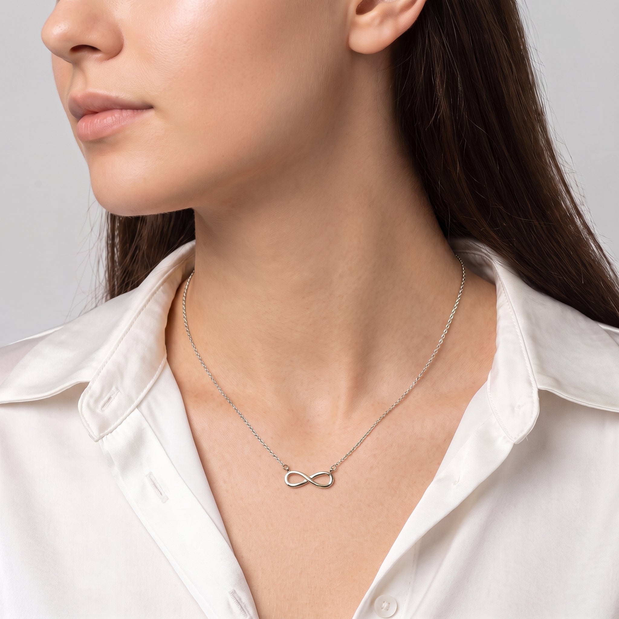 Silver infinity necklace at the collarbone, a white silk shirt