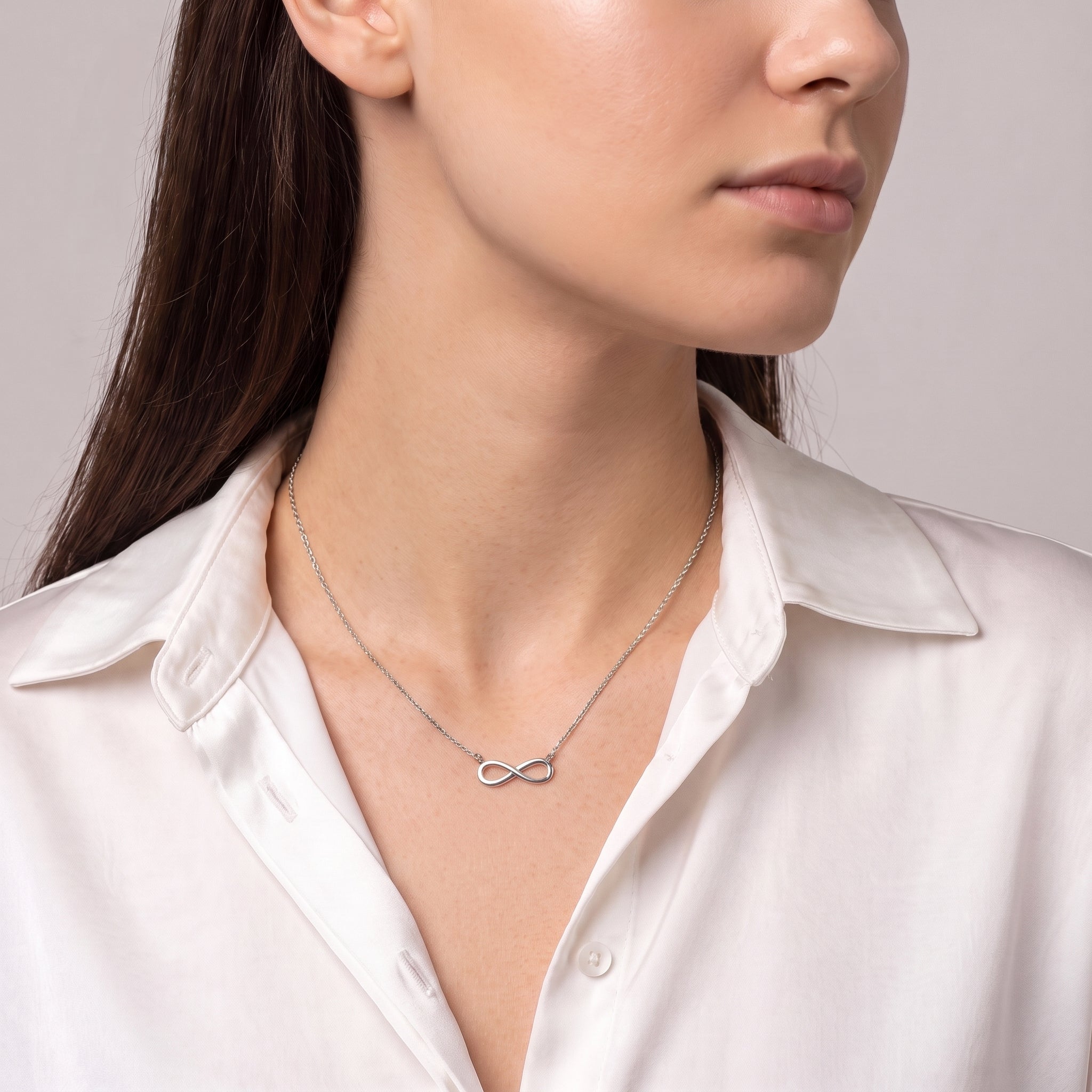 Silver infinity necklace worn with a glance over the shoulder