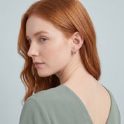 Silver coin huggie earring seen over the shoulder