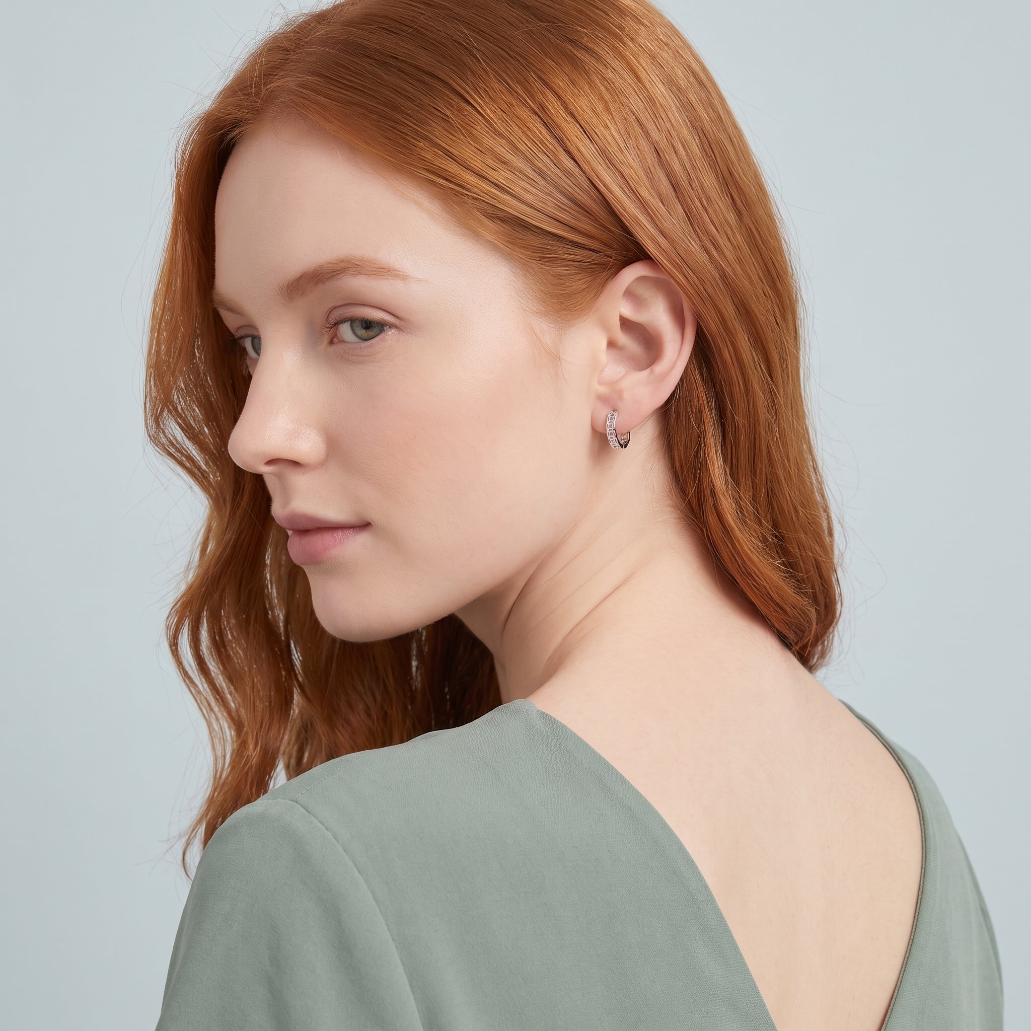 Silver coin huggie earring seen over the shoulder