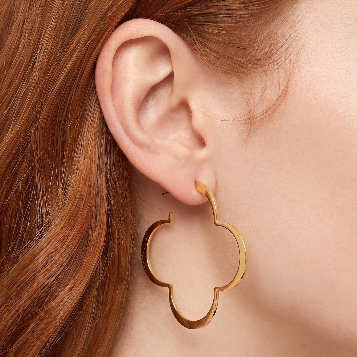 Gold clover hoop earrings, large four leaf outline, on the ear
