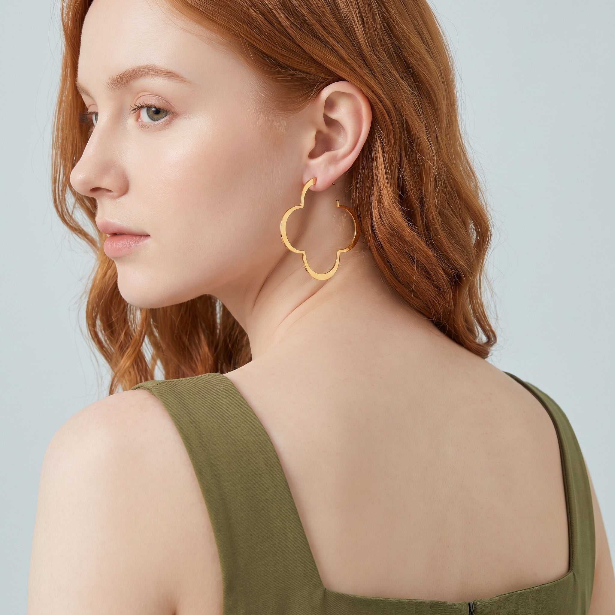 Gold clover hoop earring seen over the shoulder, olive dress