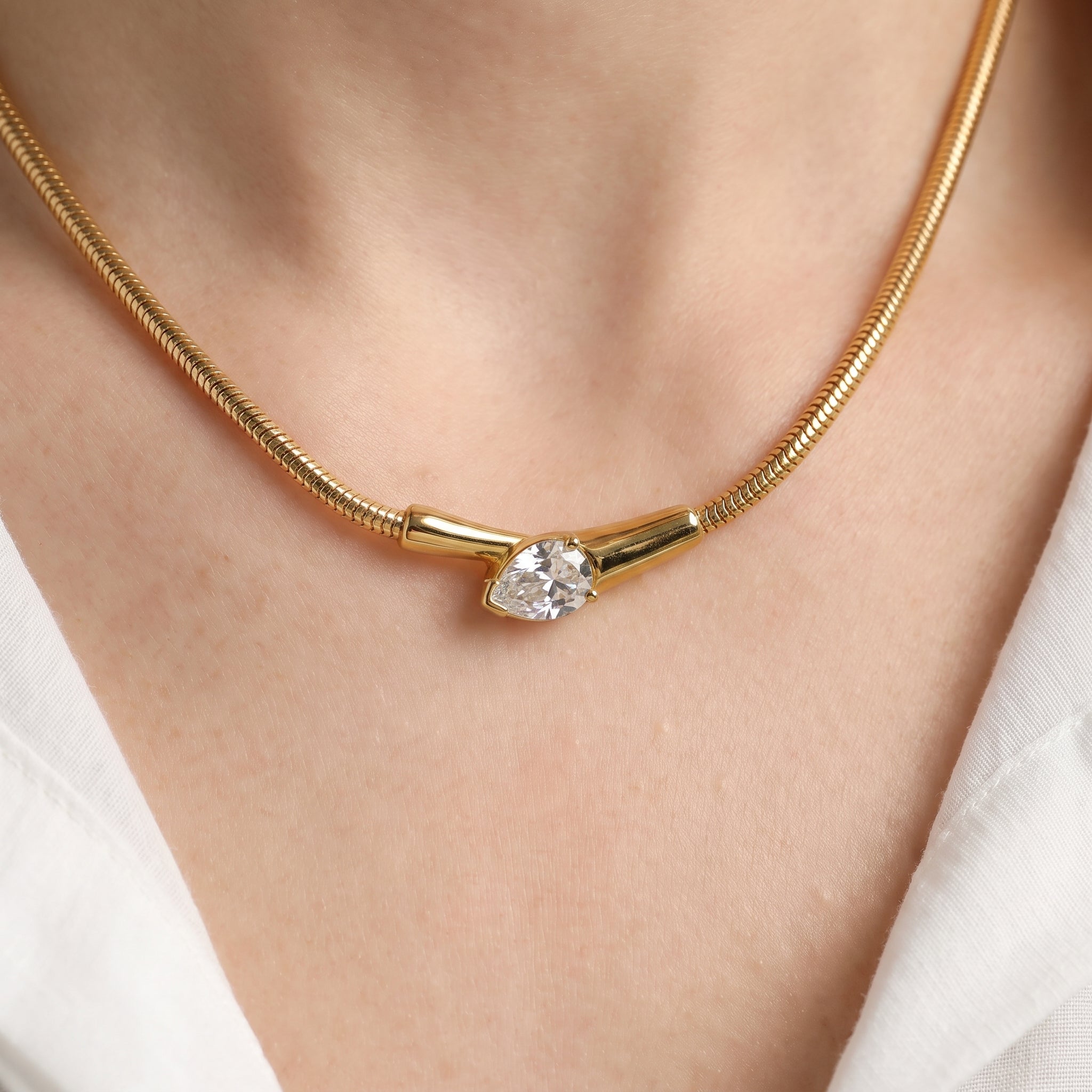 Gold snake necklace with a pear crystal snake head on skin