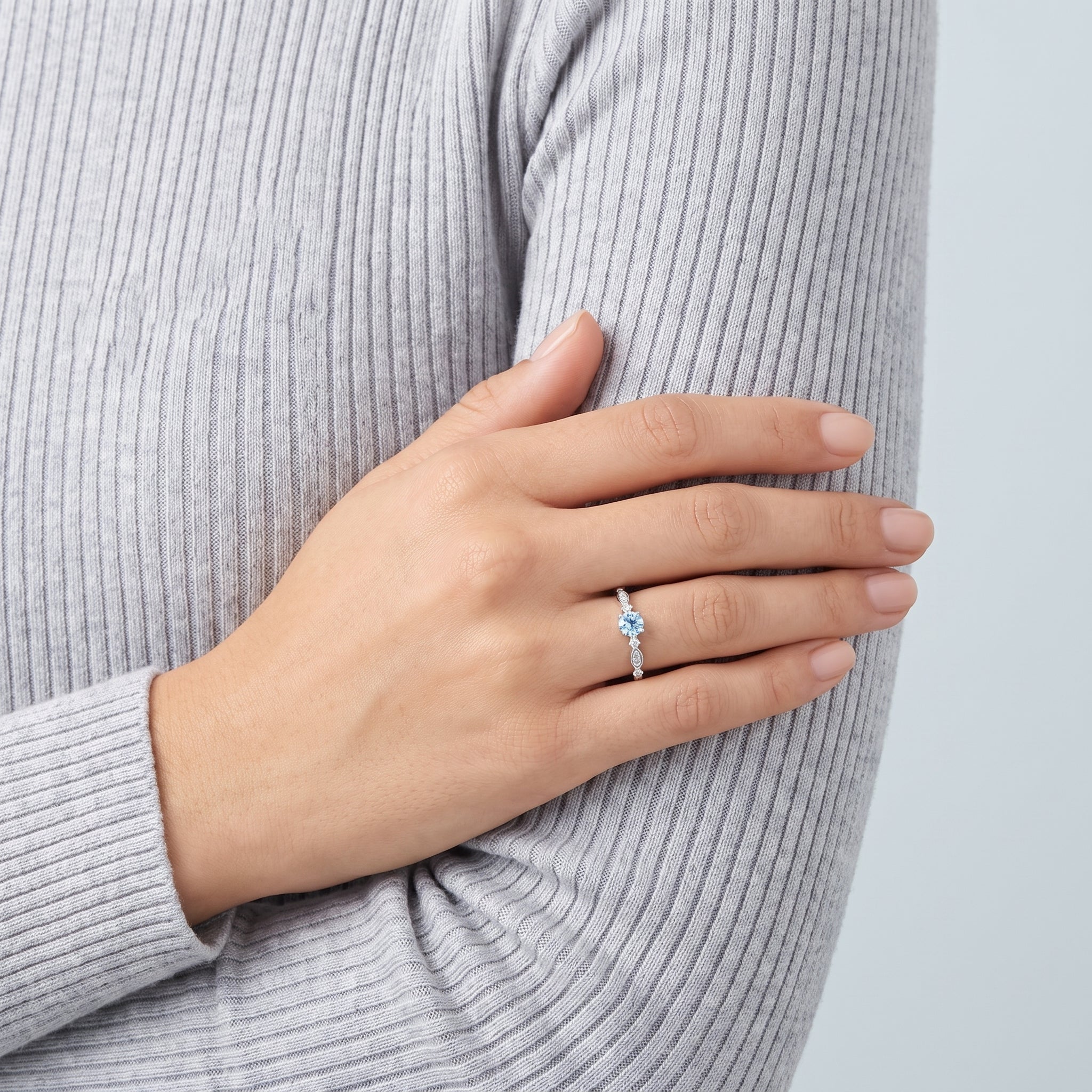 Hand on a grey knit sleeve wearing a light blue crystal ring