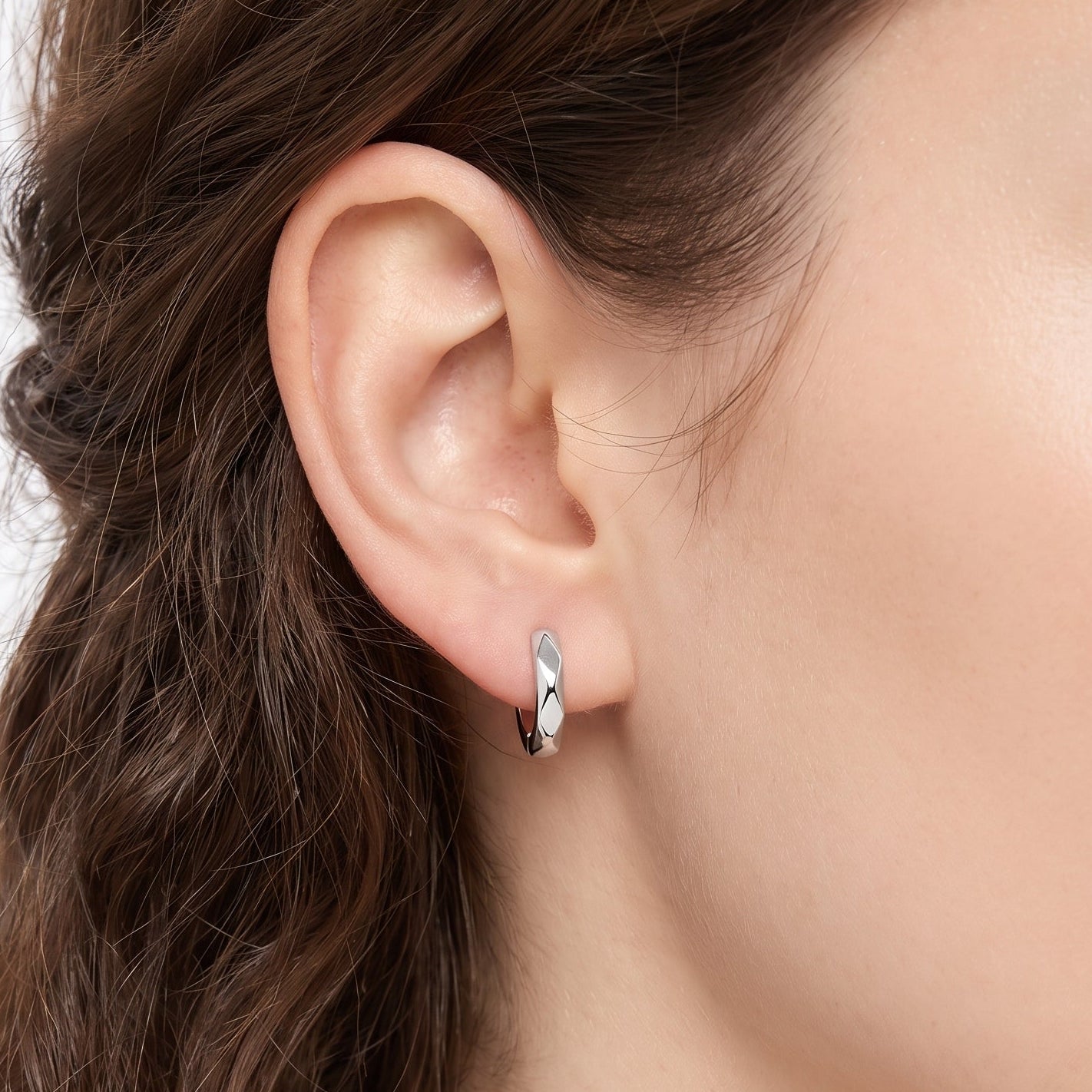 Silver faceted huggie hoop earring hugging the earlobe, close-up