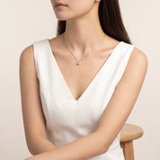 Silver solitaire necklace worn with a white V-neck top, seated