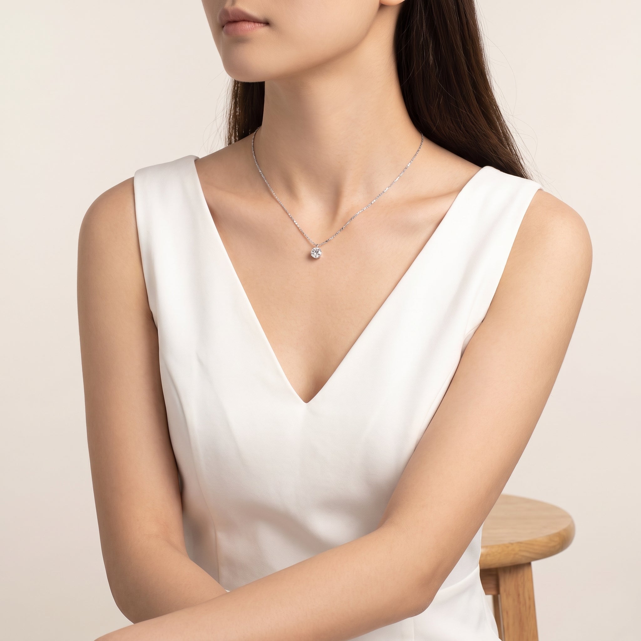 Silver solitaire necklace worn with a white V-neck top, seated
