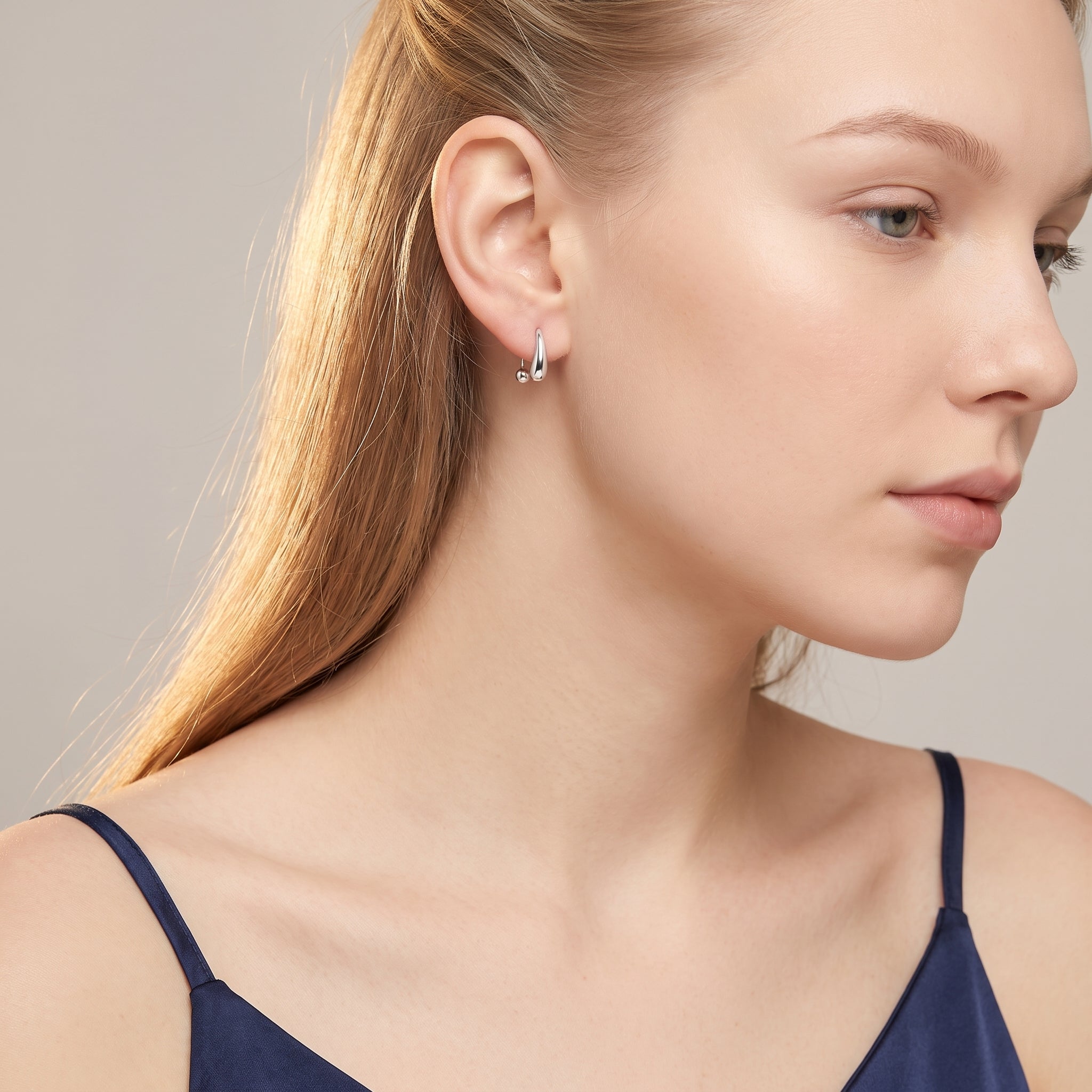 Silver teardrop hoop earring worn with a navy camisole
