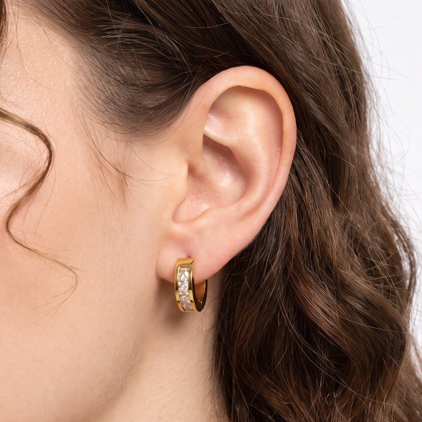 Ear wearing Navalli gold crystal huggie earring Maelle with channel-set stones