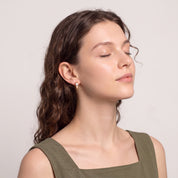 Woman with curly hair and closed eyes wearing Maelle gold crystal huggie earring
