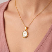 Gold initial necklace with a mother of pearl letter M pendant on skin