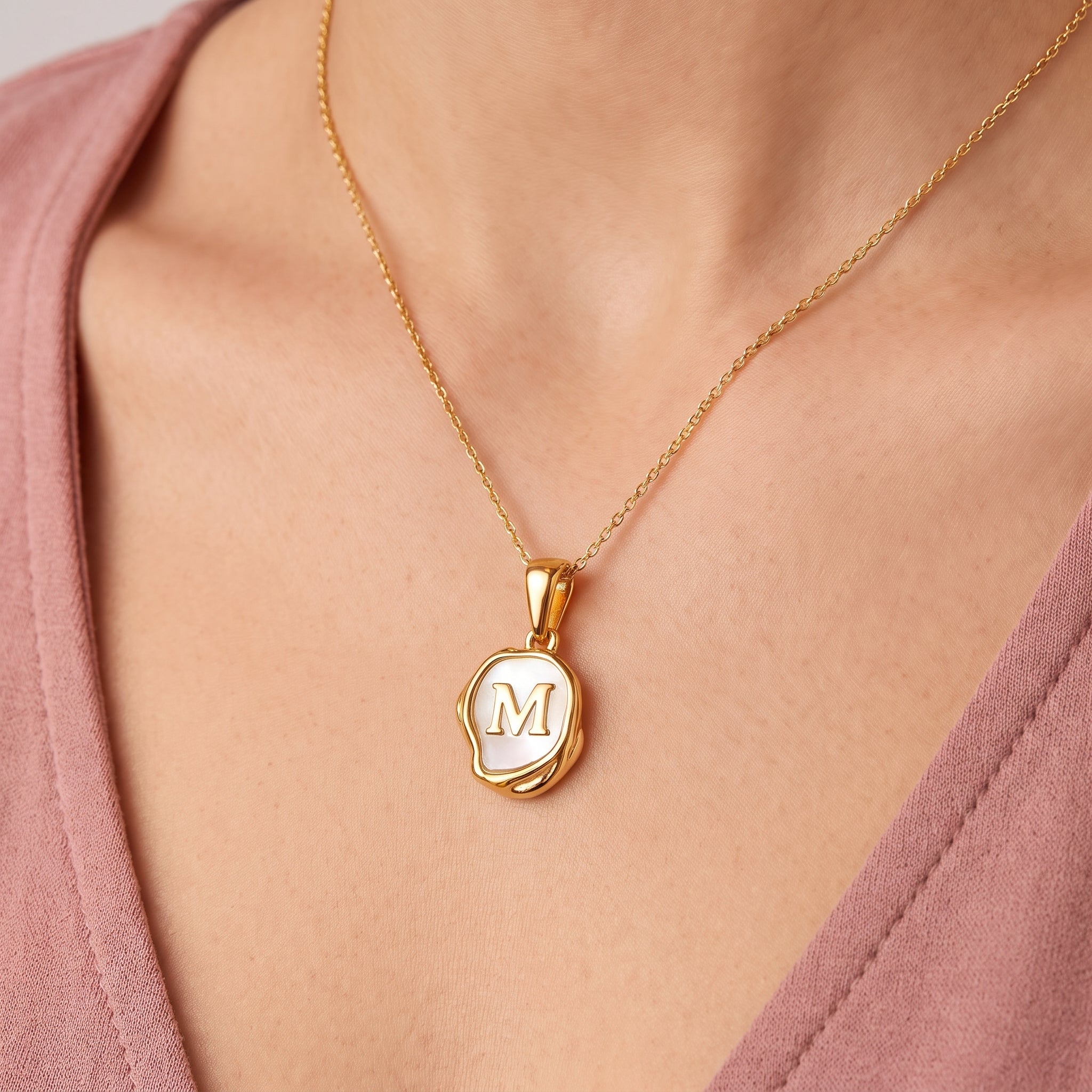 Gold initial necklace with a mother of pearl letter M pendant on skin