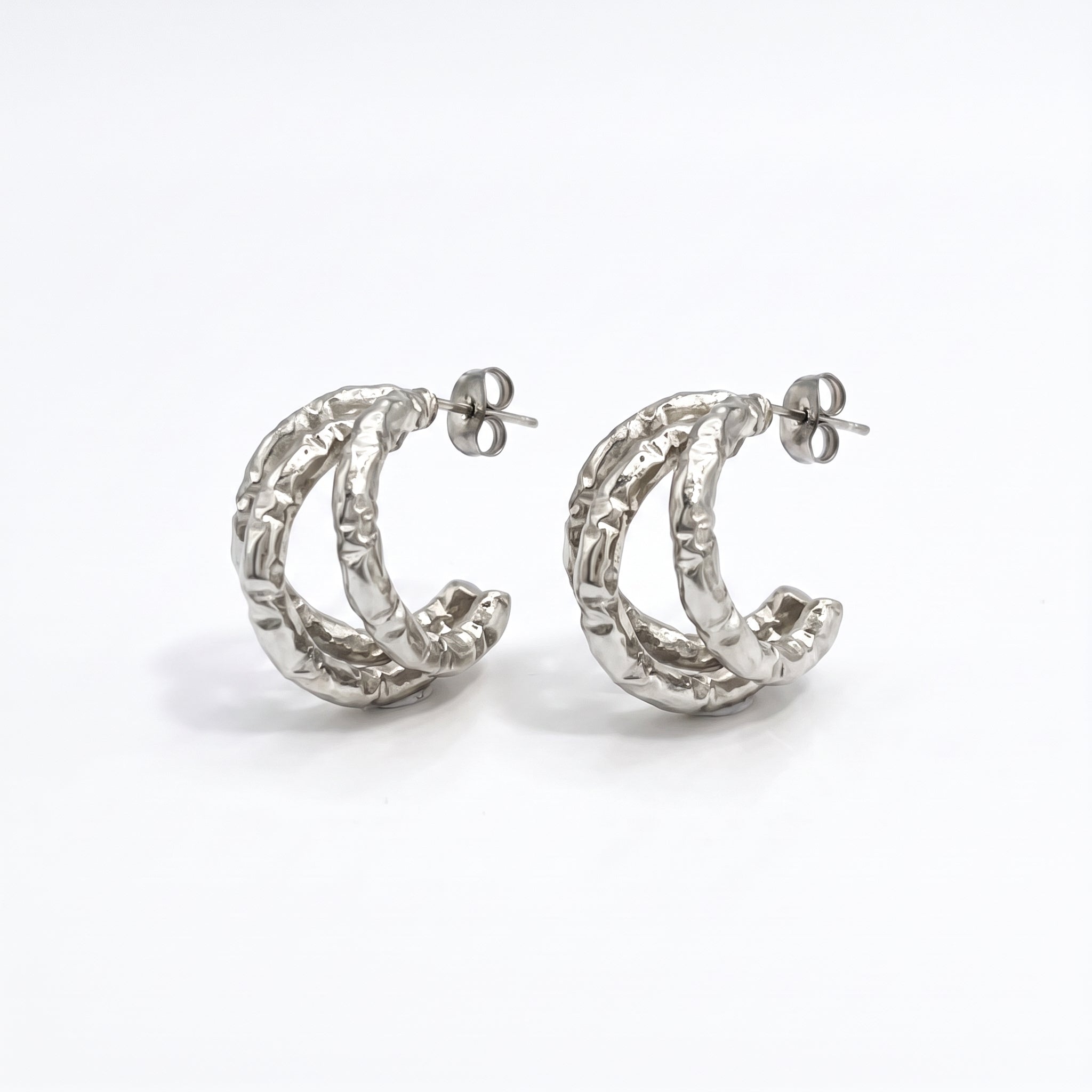 Pair of silver textured triple hoop earrings on white