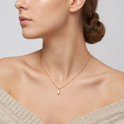 Gold bar pendant necklace on a beaded chain, worn at the neck